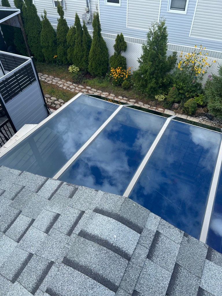 A close-up of a perfectly streak-free commercial office window, the surface glistening with a refined sheen against a tranquil, muted sky. The window’s frame displays sleek, matte black metal, with delicate architectural grooves that indicate premium quality. Beyond the glass, a hint of blurred urban skyline offers subtle context without distracting from the breathtaking transparency of the pane. Soft, natural light from a cloudy afternoon bathes the scene, creating gentle highlights and understated gradients along the window’s edges. Captured from a straight-on, eye-level perspective, the image embodies an elegant calm and professionalism, using minimalist composition and photographic detail to emphasize the expertise offered by Vitres Reflexio.
